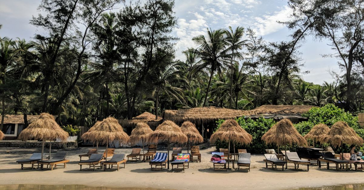 Relaxing beachside view with nipa huts and palm trees in Goa, India, perfect for a tropical getaway.