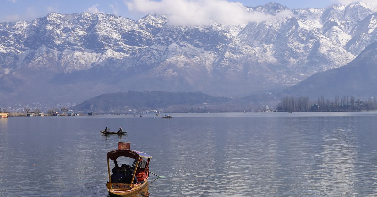 Peaceful view of Dal Lake in Srinagar surrounded by snowcapped Himalayas, featuring traditional boats.