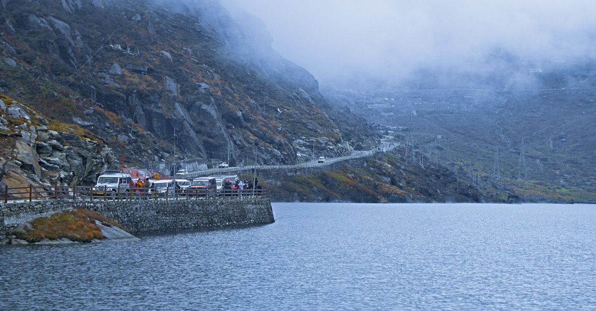 Serene winter scene at a misty lake with mountains and vehicles in Sikkim, India.