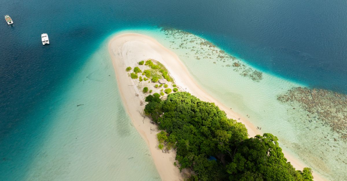 Discover the serene beauty of Jolly Buoy Island's white sandy beach and turquoise waters from above.